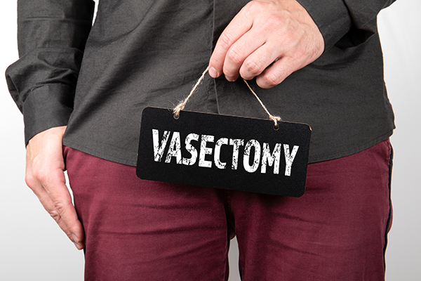 fully dressed man holding vasectomy sign in front of genital area